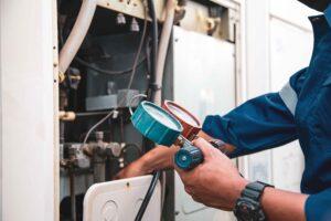 A person in a blue uniform adjusts gauges on an AC unit, focusing on cooling maintenance work in Lemoore, CA.