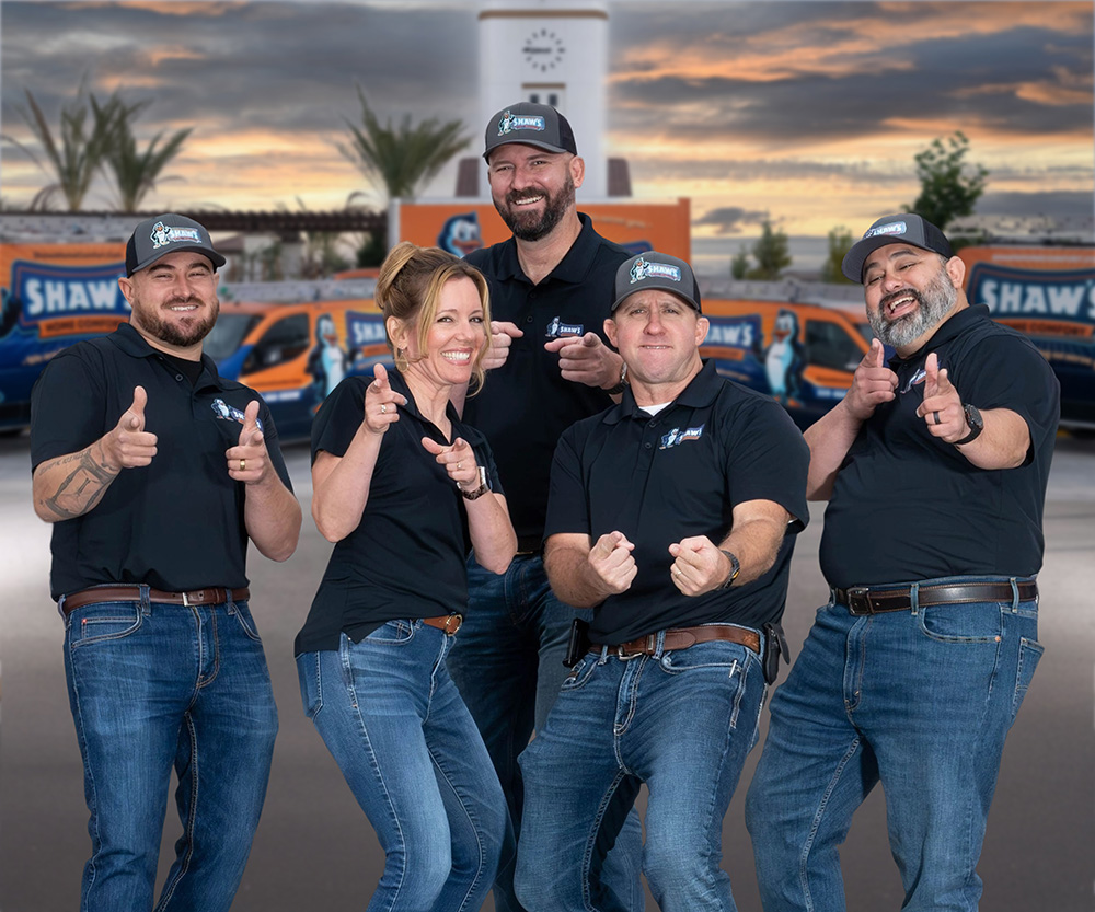 Five people in matching Shaw's uniforms stand outdoors, smile, and point finger guns at the camera, with vehicles and palm trees behind.