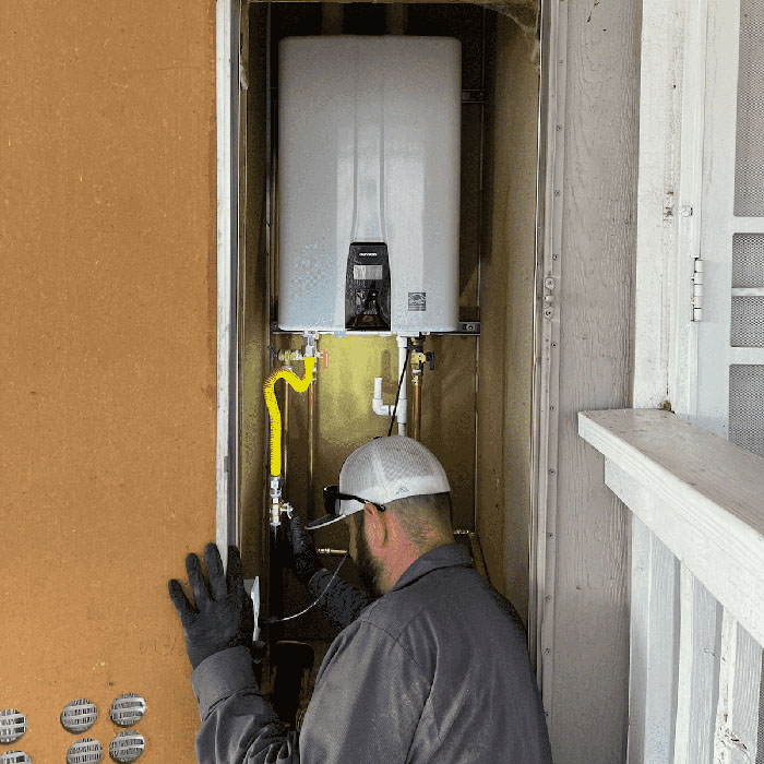A gloved, capped worker installs or inspects a water heater mounted inside a small utility closet.